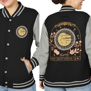 May include: Black and gray varsity jacket with a gold and white Sagittarius design on the back. The jacket has a button-up front, gray sleeves, and white and gray striped trim. A gold emblem is on the front.