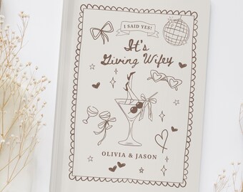 May include: A cream-colored notebook with a brown decorative border and illustrations. The cover features the text "I Said Yes!" and "It's Living Wifey" along with drawings of a martini, hearts, and disco ball. The names "Olivia & Jason" are also printed.
