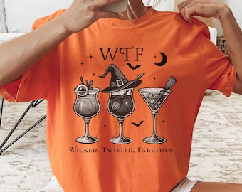 May include: Burnt orange t-shirt with a graphic of three cocktails, a witch hat, bats, and the text "WTF". Below the graphic, the text reads "Wicked, Twisted, Fabulous".