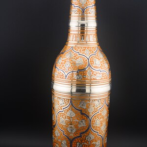 May include: A silver and orange decorative bottle with intricate floral patterns. The bottle has a narrow neck and a wide base.