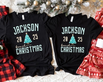 May include: Two black t-shirts with the text "JACKSON 2025 beach CHRISTMAS" in white and light blue. A light blue Christmas tree graphic is between the numbers 20 and 25. Red and black plaid pajama pants and red and white patterned pajama pants are visible.