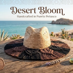 Peut inclure: Un chapeau en paille avec une calotte pincée et un large bord orné de franges en macramé noir et marron. Le texte Desert Bloom Handcrafted in Puerto Peñasco et un sceau Breezy Bohemian sont visibles sur l'image.