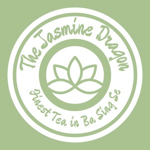 Pode incluir: Um logotipo circular branco com o texto "The Jasmine Dragon Finest Tea in Ba Sing Se" e um design estilizado de flor de lótus. O texto "茉莉" está na parte superior da imagem e o texto "三天不负莫一日茶" está na parte inferior da imagem.