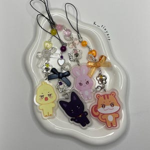 Peut inclure: Six porte-clés colorés avec différents motifs d'animaux de dessin animé, dont un poussin, un lapin, un chat et un écureuil. Chaque porte-clés a une chaîne argentée et une ficelle noire.