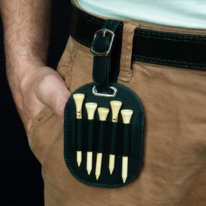 May include: A black leather golf tee holder with five wooden tees. The holder is attached to a belt loop.