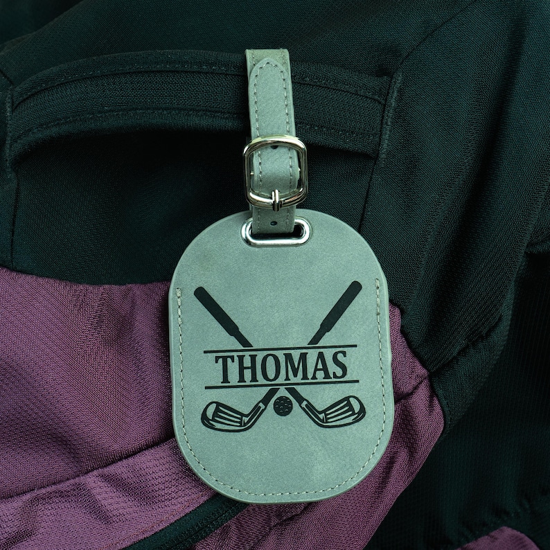 May include: Gray leather luggage tag with a golf club design and the name "THOMAS" printed on it.