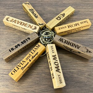 May include: A set of wooden keychains with personalized engravings. The keychains feature various messages, including "Best Mom Ever", "Drive Safe", "Olivia and Liam", and "Best Dad Ever".