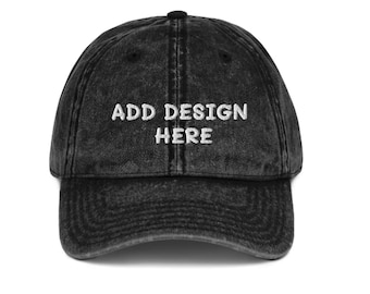 Op de afbeelding: Een zwarte baseballcap in vintage-stijl met de tekst "ADD DESIGN HERE" in het wit geborduurd. De cap heeft een gebogen klep en een knoop aan de bovenkant. Een klassiek accessoire.