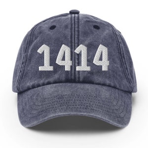May include: A navy blue baseball cap featuring the number "1414" embroidered in white. The cap has a curved peak and an adjustable strap. The fabric has a faded, vintage appearance, giving it a worn look.