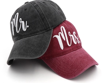 May include: Two baseball caps, one charcoal gray and one burgundy, are stacked. The gray cap has "Mr." embroidered in white script, and the burgundy cap has "Mrs." embroidered in white script. Both caps have a curved brim.