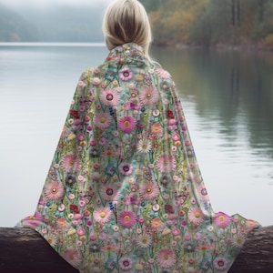 Op de afbeelding: Een bloemenpatroon deken met roze, groene en blauwe bloemen op een witte achtergrond. De deken is over een boomstam aan een meer gelegd.