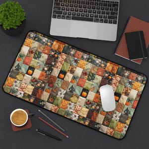 May include: A rectangular desk mat with a patchwork quilt design in autumnal colours of orange, green, and brown. The mat has a black border and is decorated with pumpkins and other fall motifs. A white computer mouse rests on the mat.