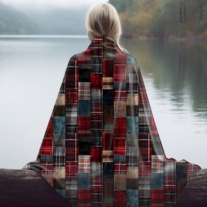 May include: A red, blue and brown plaid throw blanket with a patchwork design. The blanket is draped over a person sitting on a log by a lake.