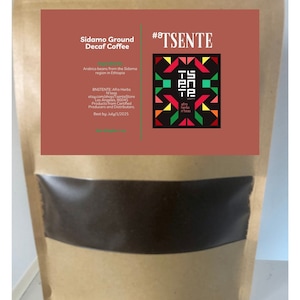 Könnte beinhalten: Ein brauner Papierbeutel mit einem Sichtfenster, das dunkelbraunen Kaffeepulver zeigt. Der Beutel trägt ein Etikett mit dem Text "Sidamo Ground Decaf Coffee" und "#8TSENTE". Das Etikett enthält auch Informationen über die Kaffeebohnen, den Hersteller und das Mindesthaltbarkeitsdatum.
