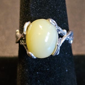 May include: A silver ring with a pale yellow oval gemstone set in a delicate, leafy design.