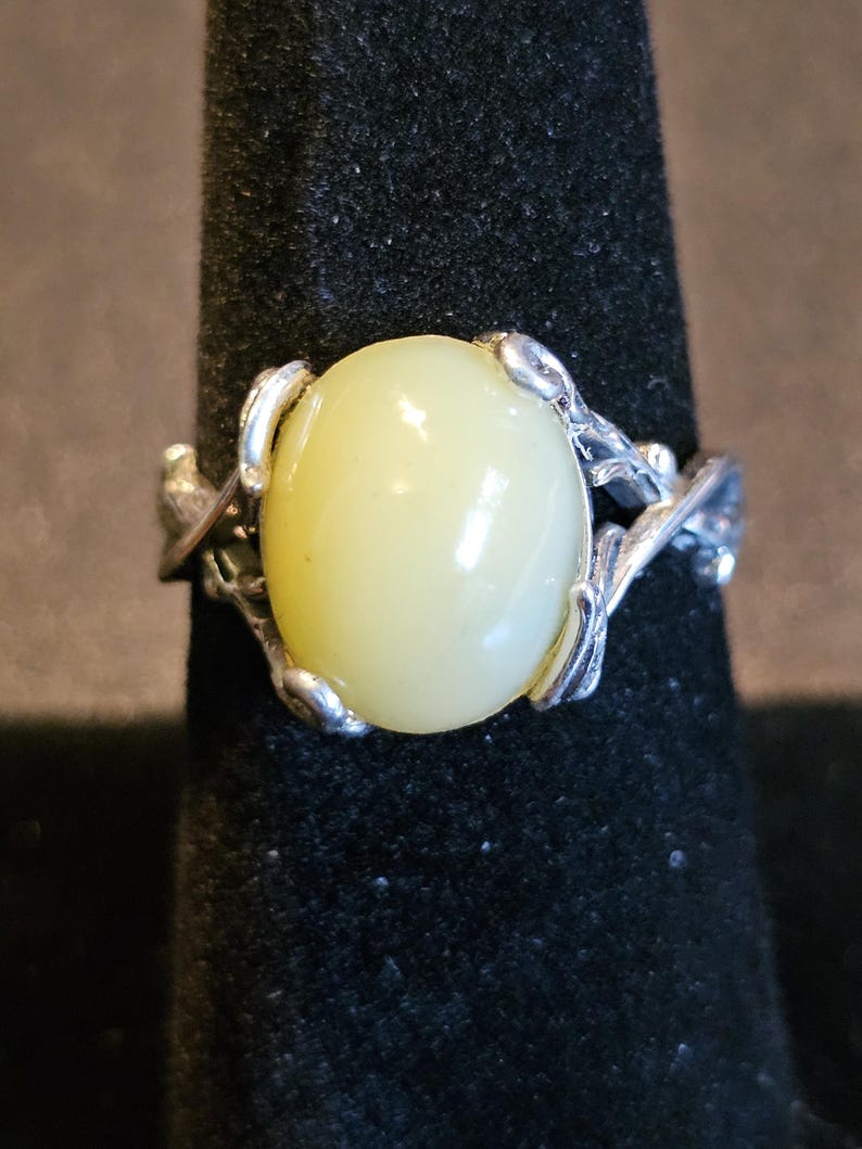 May include: A silver ring with a pale yellow oval gemstone set in a delicate, leafy design.