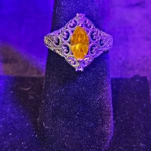 May include: A silver ring with a large, yellow, marquise-shaped gemstone set in a filigree design.