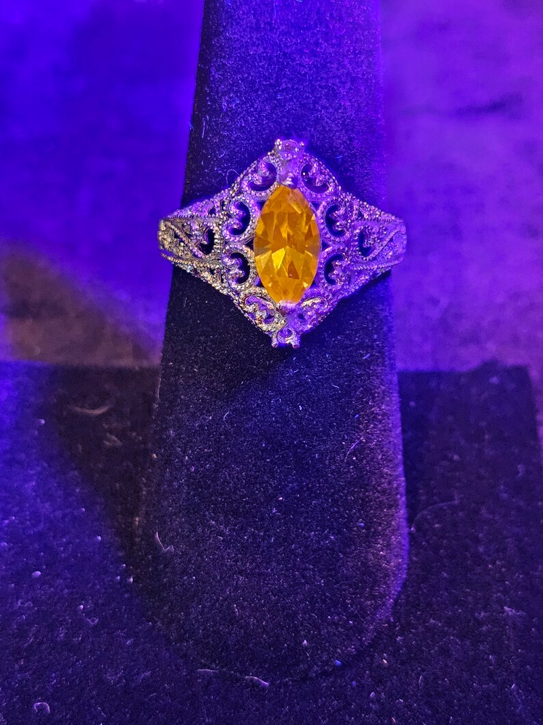 May include: A silver ring with a large, yellow, marquise-shaped gemstone set in a filigree design.