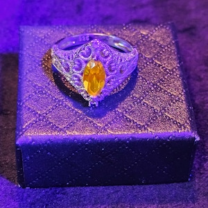 May include: A silver ring with a filigree design and a large, oval-shaped, yellow gemstone.