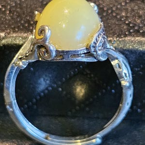 May include: A silver ring with a yellow oval-shaped gemstone set in a decorative silver setting.