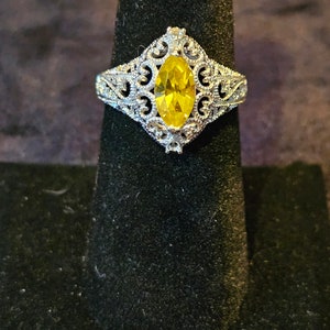 May include: A silver ring with a yellow marquise-shaped gemstone set in a filigree design.
