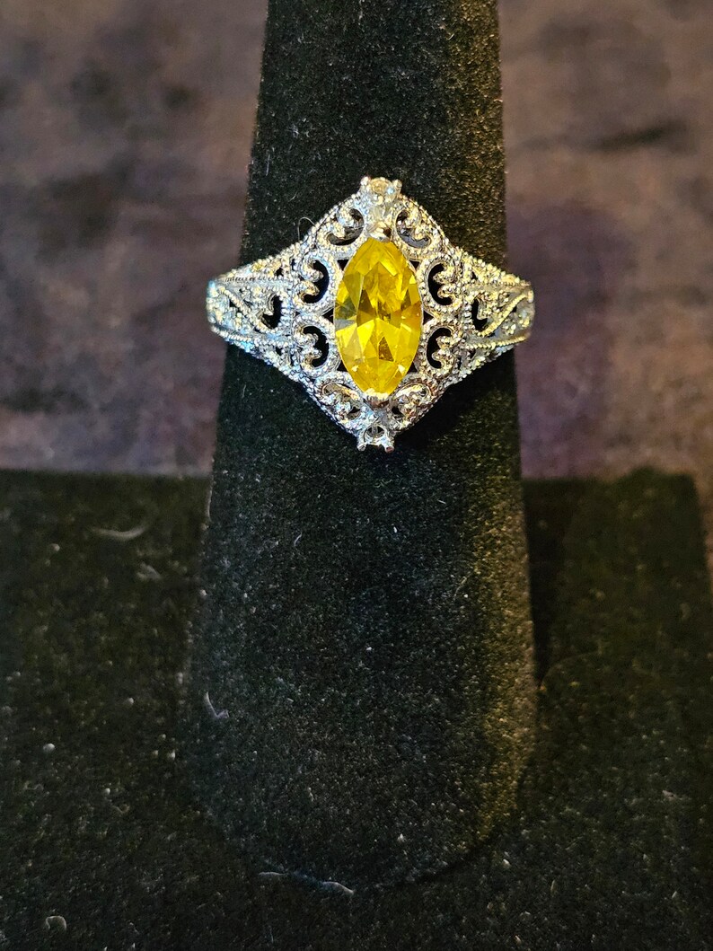 May include: A silver ring with a yellow marquise-shaped gemstone set in a filigree design.