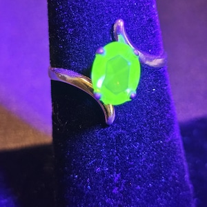Può includere: Un anello d'argento con una pietra ovale sfaccettata di colore verde brillante incastonata in un design a spirale.