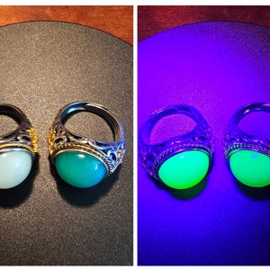 May include: Two silver rings with gold accents and oval-shaped green and white stones. The rings are shown under normal light and under a black light, revealing the stones glow green.