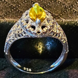 May include: A silver ring with a yellow pear-shaped gemstone set in a filigree design. The ring is marked "925" on the inside band.