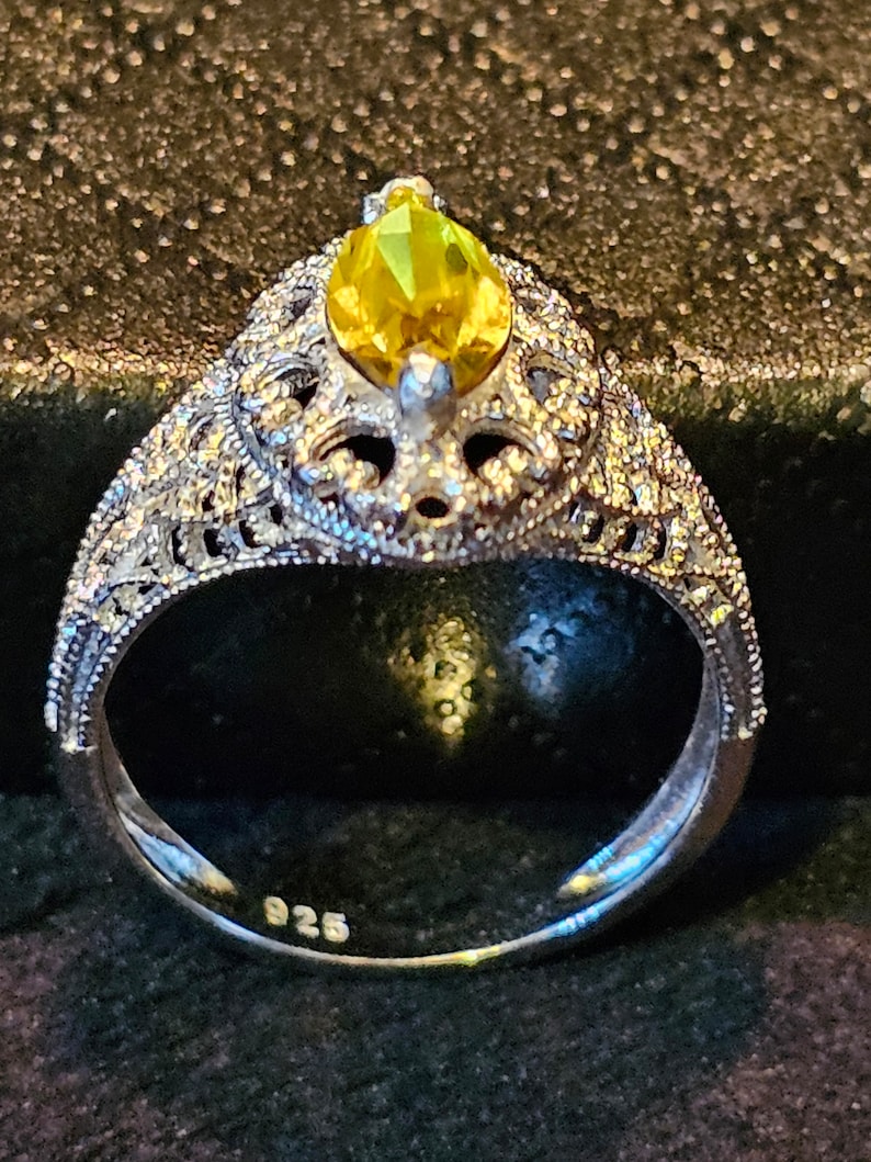 May include: A silver ring with a yellow pear-shaped gemstone set in a filigree design. The ring is marked "925" on the inside band.
