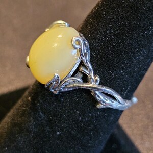 May include: A silver ring with a large, oval-shaped, pale yellow gemstone set in a delicate, leafy design.