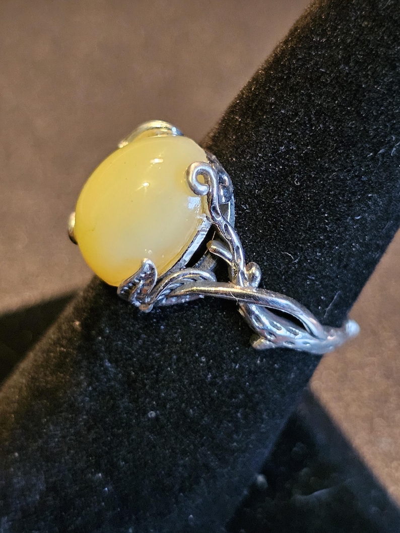 May include: A silver ring with a large, oval-shaped, pale yellow gemstone set in a delicate, leafy design.