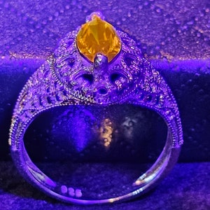 May include: A silver ring with an intricate design and a large, yellow gemstone in the center.