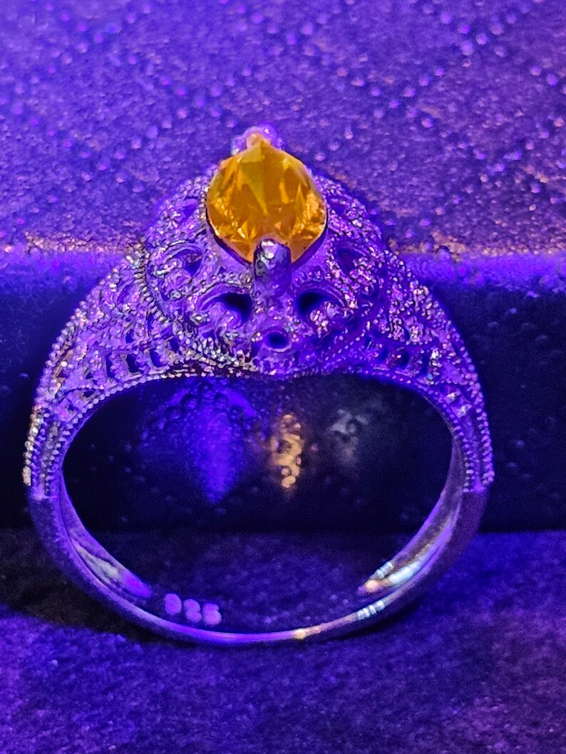 May include: A silver ring with an intricate design and a large, yellow gemstone in the center.