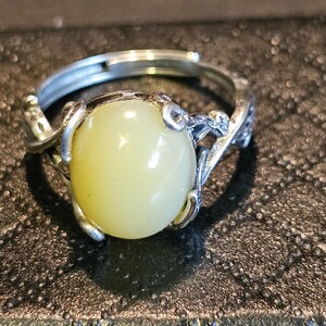 May include: A silver ring with a pale yellow oval gemstone set in a delicate, twisted silver band.