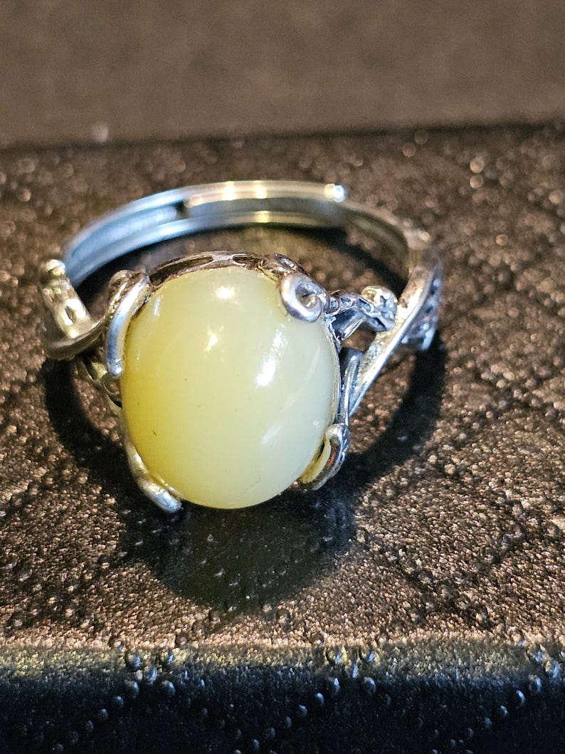 May include: A silver ring with a pale yellow oval gemstone set in a delicate, twisted silver band.