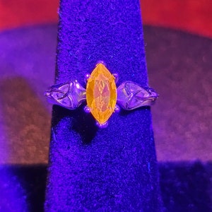 Könnte beinhalten: Ein silberner Ring mit einem großen, gelben, markisenförmigen Edelstein. Der Ring befindet sich auf einem violetten Samt-Präsentationsständer.