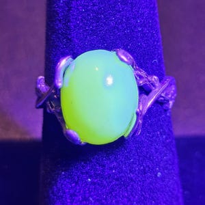 May include: A silver ring with a large, round, bright green, translucent stone set in a twisted branch design.