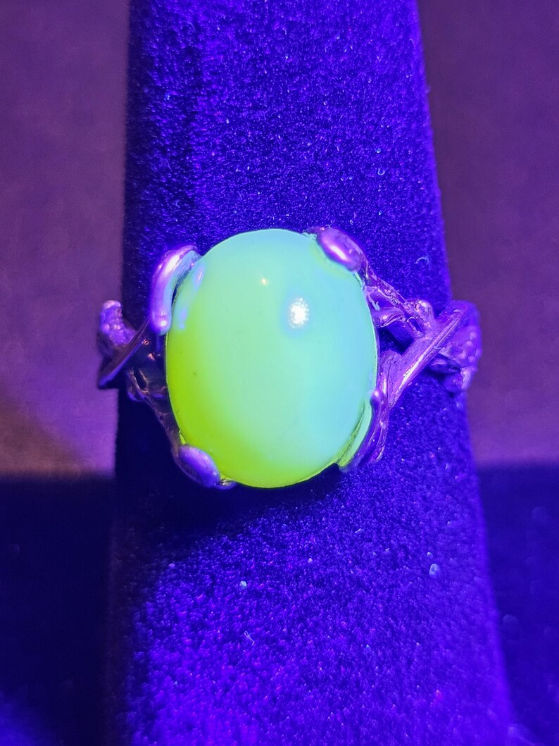 May include: A silver ring with a large, round, bright green, translucent stone set in a twisted branch design.