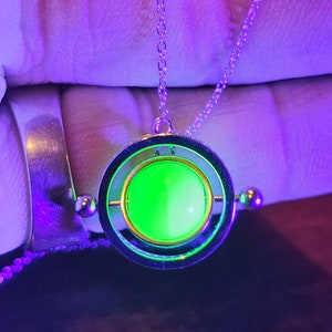 Puede incluir: Un collar de plata con un colgante giratorio que presenta un orbe de vidrio verde rodeado de círculos concéntricos.