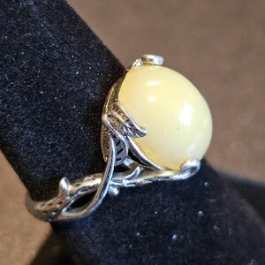 May include: A silver ring with a large, pale yellow oval gemstone set in a delicate, leafy design.