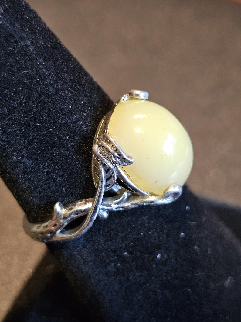 May include: A silver ring with a large, pale yellow oval gemstone set in a delicate, leafy design.