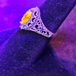 May include: A silver ring with a large, oval-shaped yellow gemstone set in a filigree design.