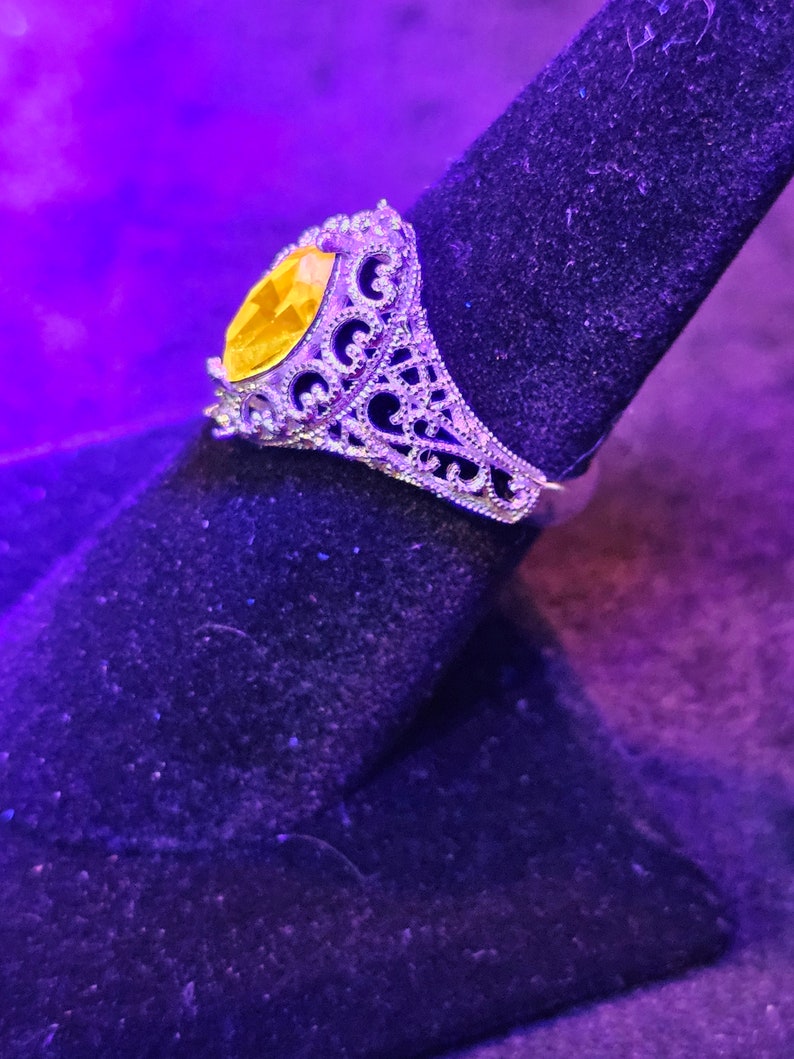 May include: A silver ring with a large, oval-shaped yellow gemstone set in a filigree design.