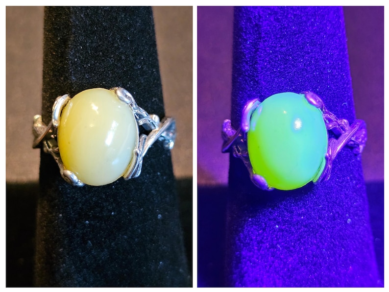May include: A silver ring with a pale yellow oval gemstone set in a delicate, leafy design. The stone glows a bright green under a UV light.