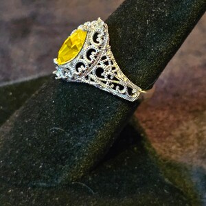 May include: A silver ring with a large, yellow, marquise-shaped gemstone set in a filigree design.