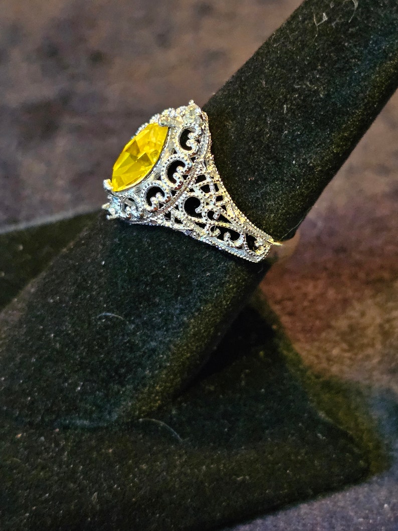 May include: A silver ring with a large, yellow, marquise-shaped gemstone set in a filigree design.