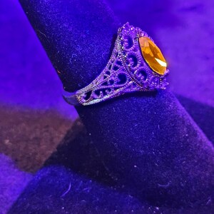 May include: A silver ring with an intricate filigree design and a large, oval-shaped, amber-colored gemstone.