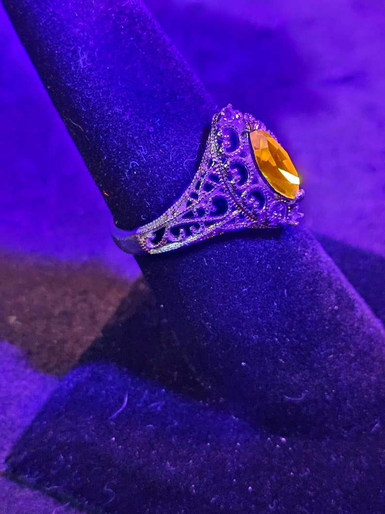 May include: A silver ring with an intricate filigree design and a large, oval-shaped, amber-colored gemstone.