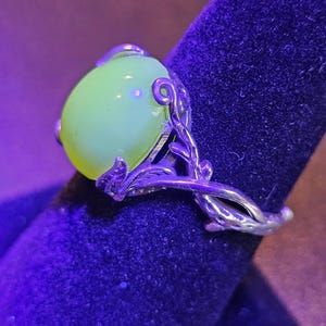 May include: A silver ring with a large, round, pale green gemstone set in a delicate, leafy design.